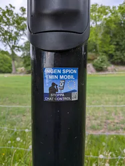 Square blue sticker protesting EU surveillance. Features a silhouette with binoculars, a smartphone displaying an eye, and the EU flag. Includes Swedish text and a QR code.