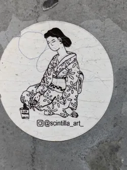 Street sticker A round sticker featuring a monochrome drawing of a woman in a kimono, sitting calmly with her eyes closed.  The style is reminiscent of traditional Japanese woodblock prints.  The artist's Instagram handle is visible on the sticker. There's a small, partially visible paint can at her feet.