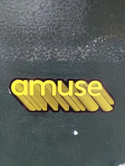 The sticker features the word "amuse" in a bold, layered, yellow font on a black background. The style is reminiscent of 70s graphic design.