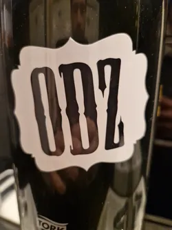 A black and white sticker with the letters ODZ in a stylized font. The sticker is rectangular with slightly curved edges and is placed on a dark surface.