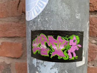 Street sticker The sticker features graffiti-style pink lettering with a green outline alongside a "My Little Pony" character with a psychedelic eye. The sticker is placed on a pole.