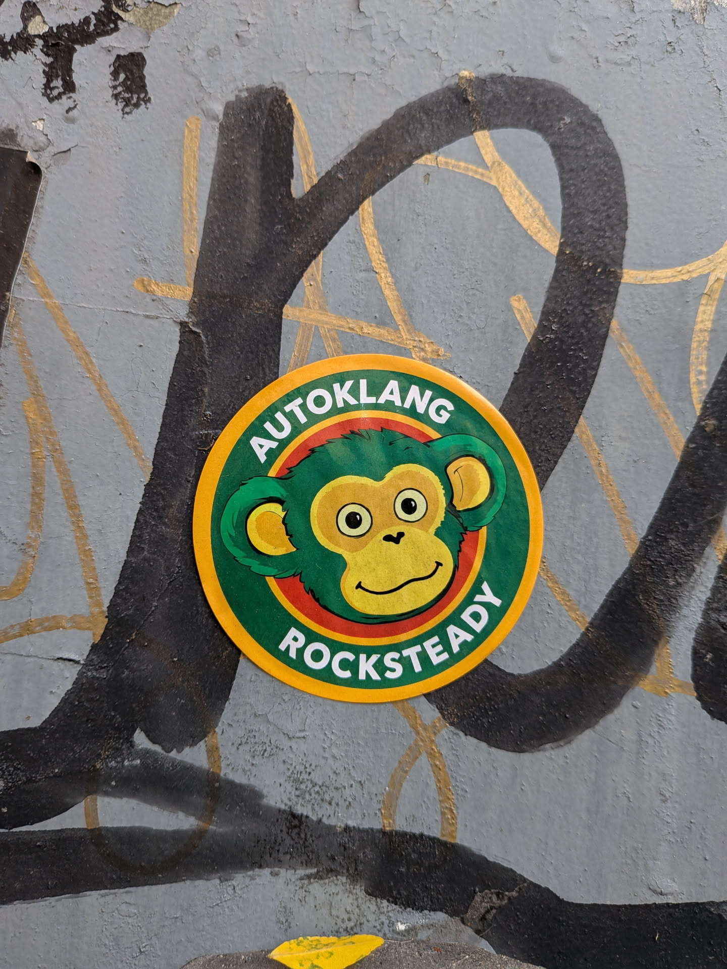 A circular sticker with a yellow outer border. The central design features a cartoon monkey head with green fur, a yellow face, and a friendly expression, set against a green background. A thin red ring outlines the monkey's head. Arched along the top in white capital letters is the word 'AUTOKLANG', and along the bottom is the word 'ROCKSTEADY'.