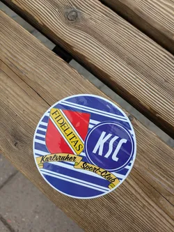 Street sticker A round sticker featuring the logo of Karlsruher Sport-Club (KSC), a German football club. The logo includes the club's name, the abbreviation KSC in a circle, and the word "Fidelitas" (Latin for "faithfulness") on a shield. The colors are mainly blue, red, and yellow.