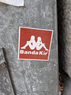 Street sticker Square red sticker with a white border. Features a white silhouette parody of the Kappa logo, depicting two figures sitting back-to-back holding bottles, above the white text 'Banda Kir®'.