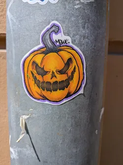 Street sticker Die-cut sticker of an orange pumpkin with a menacing skull face, dark stem, purple outline, and the tag 'MOWE'.