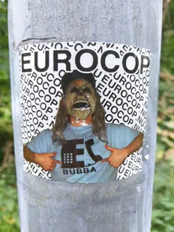 Street sticker Sticker featuring a person wearing a mask, pointing at a logo on their shirt that says 'Bubba'. The background is filled with the word 'Eurocop' repeatedly. 