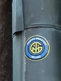 Street sticker A round sticker with a logo featuring the letters 'NG' intertwined, the number '93', and the word 'MILANO' at the bottom. The logo is in yellow and gold, and it is set against a blue background. The text 'GRUPPO IMBASTISCI' is printed above the logo.