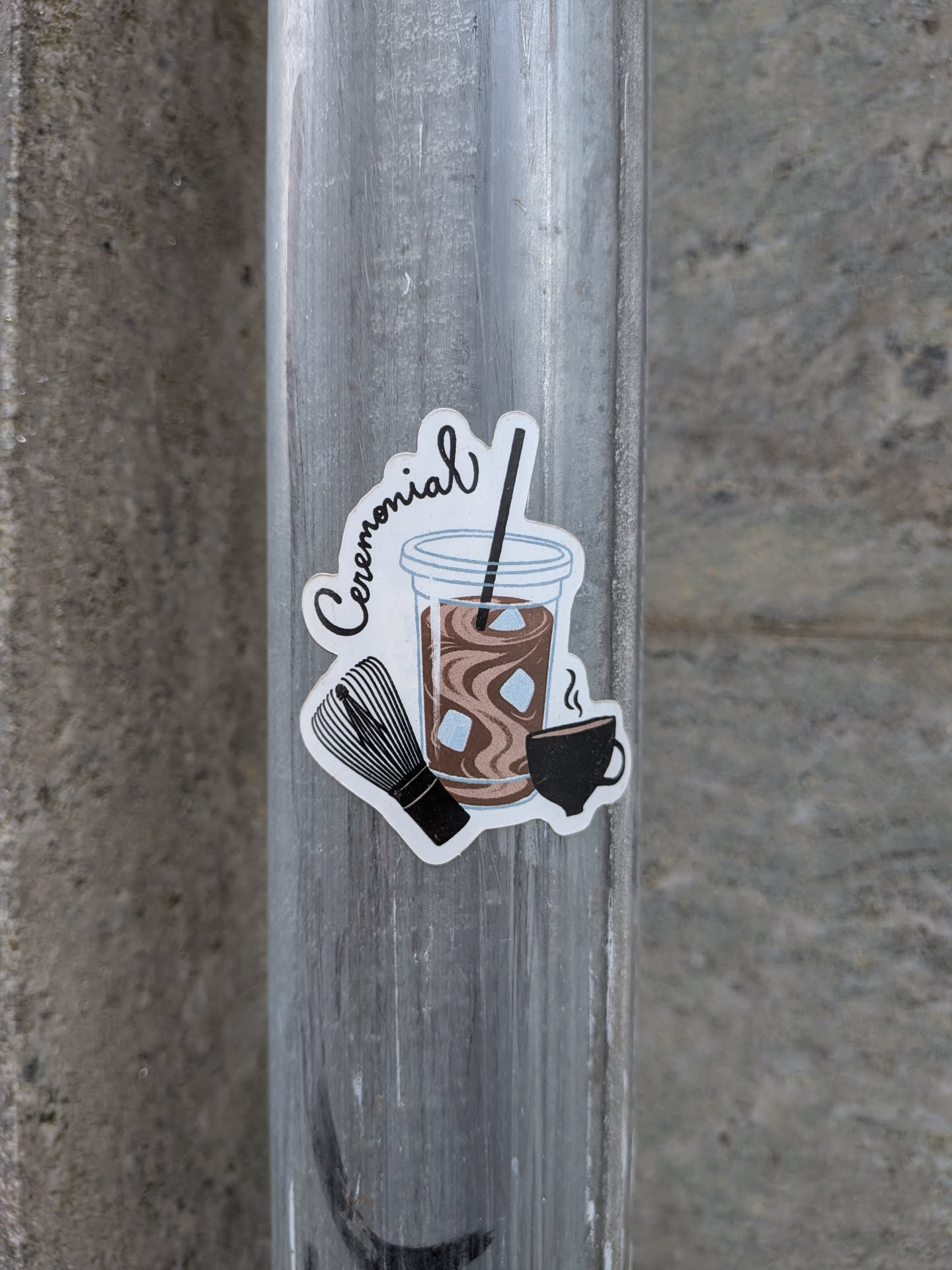 A die-cut sticker depicting an iced brown latte in a plastic cup with a straw, a bamboo tea whisk, and a small steaming black cup. The word 'Ceremonial' is written in cursive script at the top.