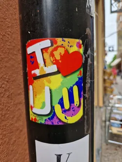 Street sticker This sticker features a vibrant design with the words "I love you" in a playful font. The colors are bright and bold, and the overall style is reminiscent of street art or graffiti.  A hand gesture is displayed expressing positivity.
