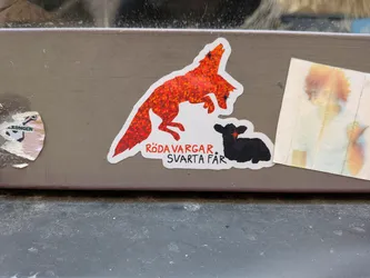 Street sticker A die-cut sticker depicting a sparkling, red holographic wolf in mid-leap above a silhouette of a black sheep. Below them is the Swedish phrase 'RÖDA VARGAR, SVARTA FÅR' in red and black lettering. Both animals feature stylized star-shaped eyes.
