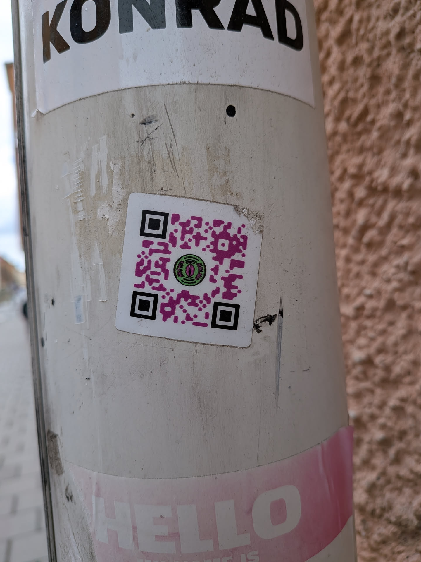 A square-shaped sticker with a white border, featuring a prominent QR code. The QR code pattern is rendered in a bright magenta color against the white background. At its center, there is a circular logo depicting a stylized green eye with a black pupil, surrounded by a black outline. The eye has a somewhat reptilian or alien appearance. Around the eye, in very small white text on a black background, are the words 'MONEY STUFF'.