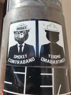 Street sticker A sticker featuring a bear wearing a Smokey the Bear hat with a marijuana leaf emblem. The text 'Smokey Contraband' is written below the bear on one side, and its mirror image on the other. 