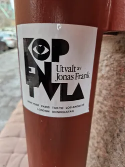 Street sticker The sticker features a geometric design incorporating an eye with a heart in its center. The text below indicates it was curated by Jonas Frank and lists various cities: New York, Paris, London, Tokyo, Los Angeles, and Bondegatan.