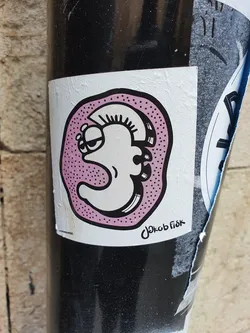 A quirky character with a mohawk, encased in a pink dotted circle. The sticker has a hand-drawn aesthetic and is signed by the artist.