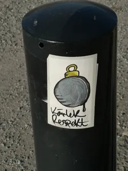 Street sticker A rectangular sticker with a white background, featuring a stylized, cartoon-like bomb. The bomb is a dark grey sphere with visible brushstrokes, outlined in thick black, and has a bright yellow fuse loop at the top, also outlined in black. A black drip extends from the bottom of the bomb. Below the bomb, in a bold, handwritten-style black script, are the words "Kärlek Respekt". The sticker is placed on a black, cylindrical bollard and shows slight wear and curling at the edges.