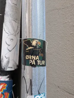 Street sticker A rectangular sticker showing a bald eagle perched on a black steam locomotive. The background has dark green and black vertical stripes. Below the illustration, the text 'ØRNA PÅ TUR' is written in bold cream lettering.