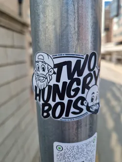 Street sticker A sticker featuring the logo of Two Hungry Bois, a food business. The logo has cartoonish illustrations of two bearded men with the text 'Two Hungry Bois'.  There is also a website address and social media instruction at the bottom.