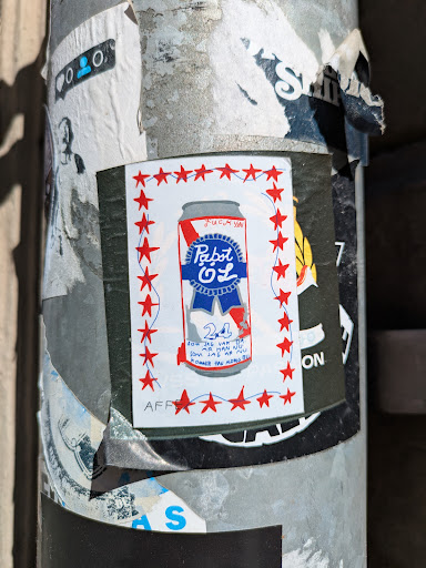 A sticker featuring a drawing of a Pabst Blue Ribbon can with a red, white, and blue color scheme. The can is surrounded by a border of red stars. Text is on the sticker and the artist signature appears to be AFF.