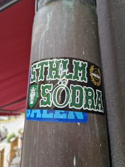 A sticker featuring the text "STHLM SÖDRA DALLEN" in green and blue.  The design includes a crest-like image and a laurel wreath.