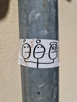 A sticker featuring a simple drawing of three faces with different expressions attached to a thin stick.  The style is minimalistic and somewhat quirky.