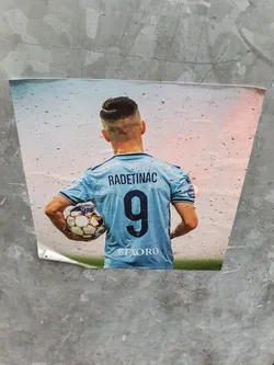 Street sticker A sticker featuring the back of a soccer player's jersey. The name "RADETINAC" and the number "9" are clearly visible. The player is holding a soccer ball. The sticker appears to be affixed to a concrete surface.