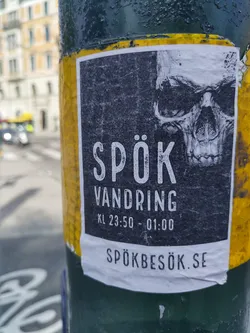 A sticker advertising a ghost walk in Swedish. The sticker features a skull graphic and the text "SPÖK VANDRING KL 23:50 - 01:00 SPÖKBESÖK.SE".