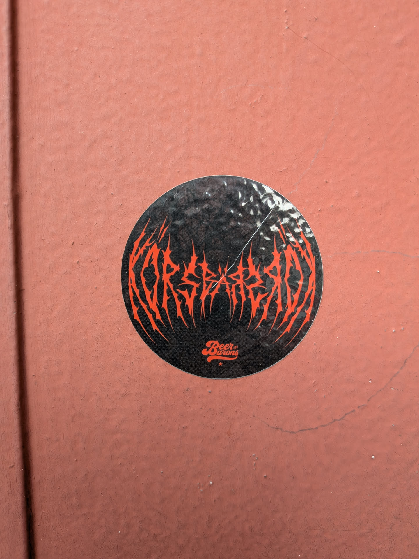 A circular black sticker on a textured red wall. It features spiky red death-metal style text reading 'KORSEARZADA' and a smaller 'Beer Barons' logo below.