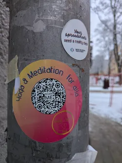 Street sticker A circular sticker featuring a vibrant gradient background, transitioning from yellow-orange at the top to a deep pink-magenta at the bottom. The sticker is adorned with small water droplets, suggesting outdoor exposure. Around the top arc, the text "Yoga & Meditation for alla" is written in a stylized font with a subtle 3D effect, appearing in shades of blue and purple. A prominent black and white QR code occupies the center, with the words "SCAN ME" embedded within it. At the bottom, a golden outline logo depicts a heart encompassing a figure in a yoga pose, with the text "GOLDEN HEART YOGA" beneath it.