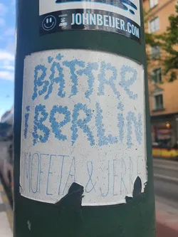 Street sticker A sticker with the text "BÄTTRE I BORLÄN" written in light blue stylized lettering. Below it, it says "MOFETA & JENNE". The sticker is slightly damaged around the edges.