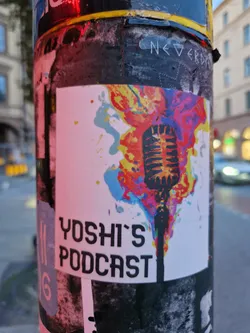 A colorful sticker advertising Yoshi's Podcast. The design features a microphone engulfed in flames with abstract paint splatter. The text 'Yoshi's Podcast' is clearly visible at the bottom.