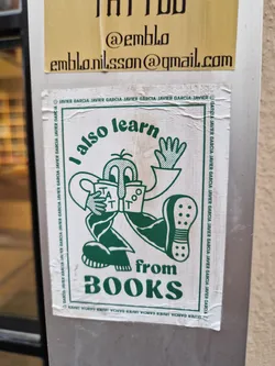 Street sticker A sticker featuring a cartoon character reading a book with the text "I also learn from BOOKS". The sticker has a green and white color scheme and a minimalist design.  The artist's email is visible on a sticker above this one.