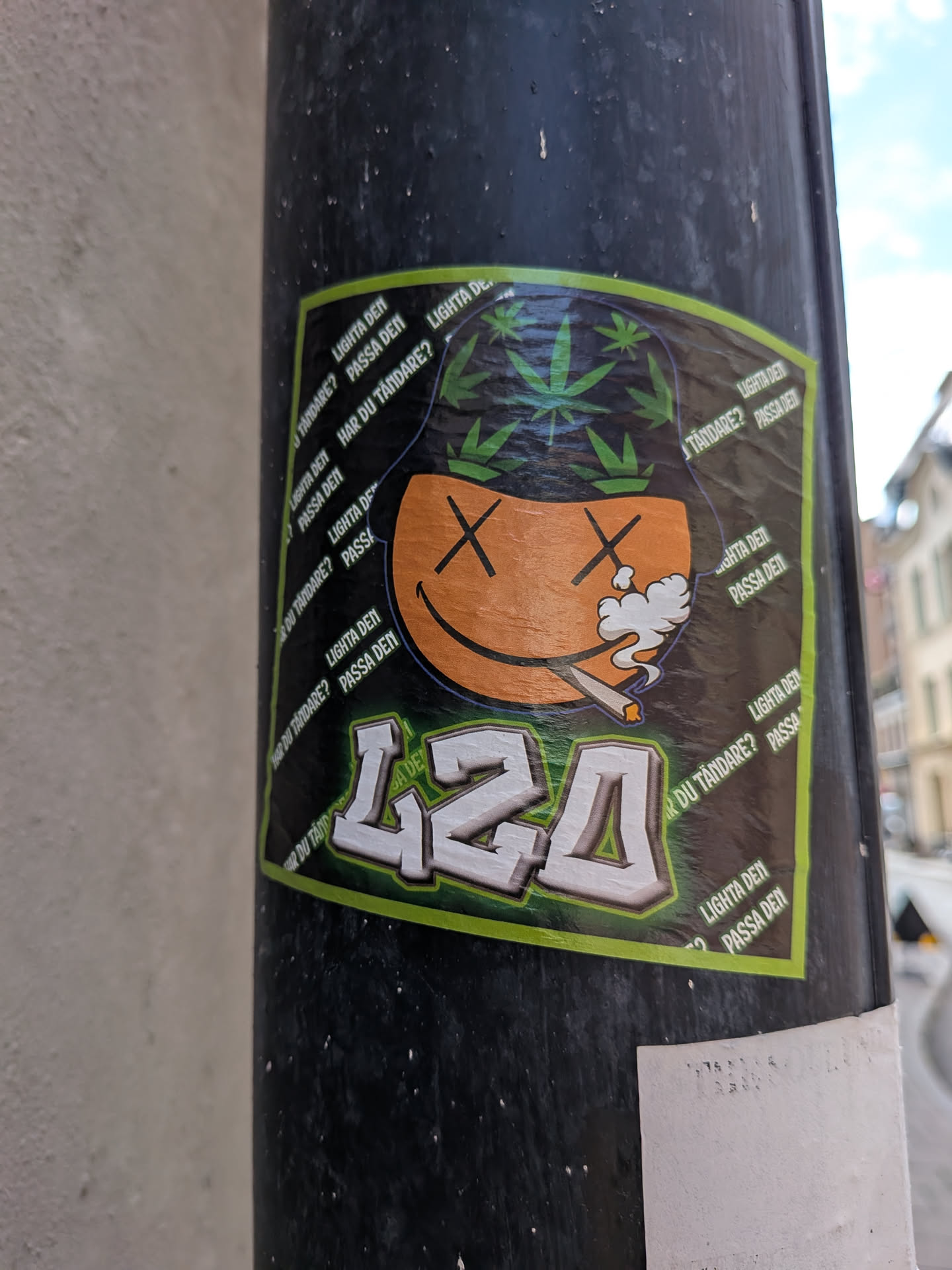 A square sticker with a green border depicting an orange smiley face with 'X' eyes smoking a joint. The character wears a black bucket hat decorated with green cannabis leaves. Below is the stylized text '420' in white and green. The dark background features repeating Swedish phrases like 'LIGHTA DEN' and 'PASSA DEN'.