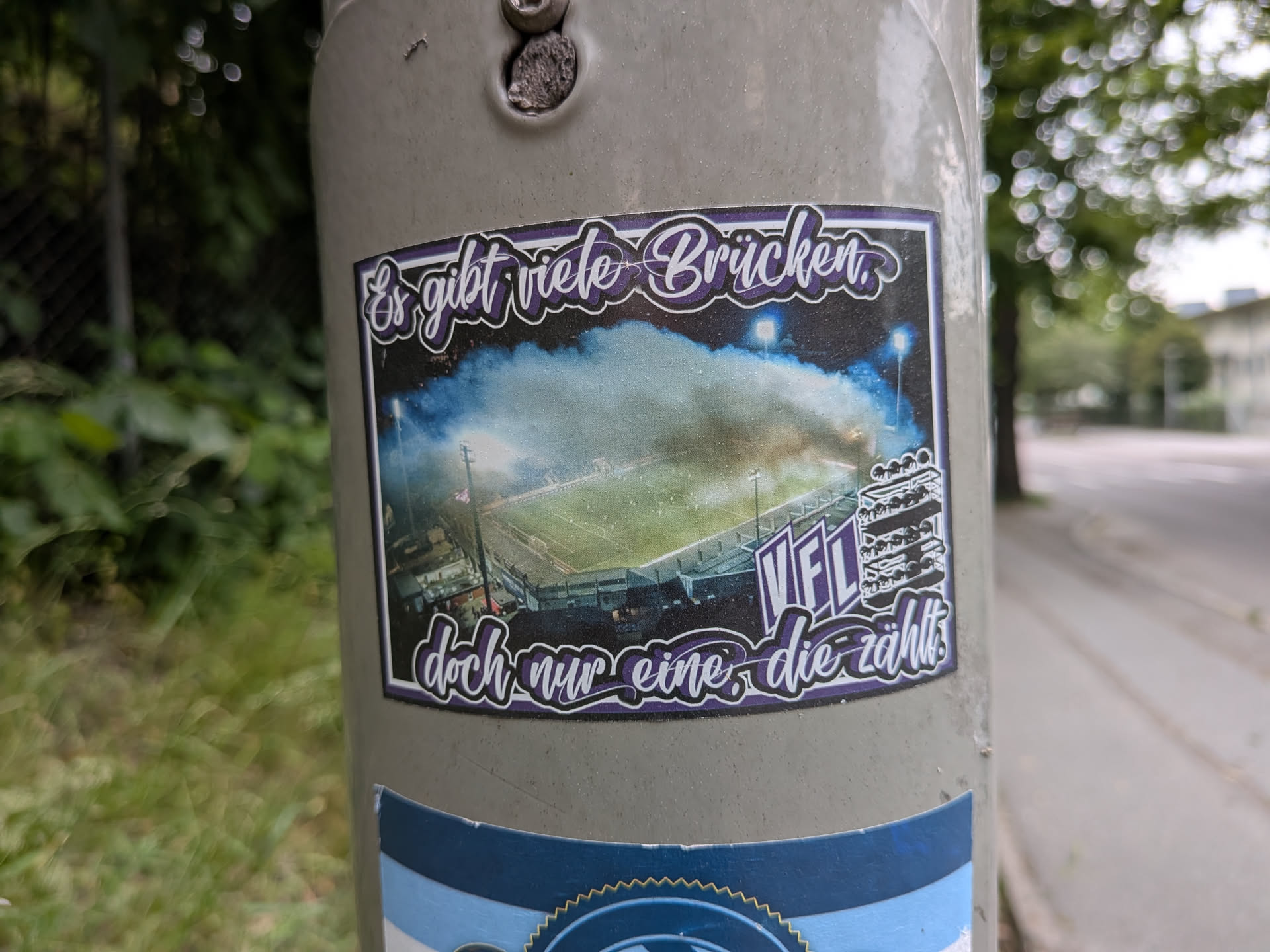 Rectangular sticker depicting an aerial view of a football stadium at night filled with blue smoke. Features purple cursive German text at the top and bottom, with 'VfL' and a stadium graphic in the bottom right corner.
