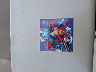 The sticker is a square-shaped collage set against a dark blue background. Dominating the center-right is a realistic human face, appearing to be a man with light hair, looking directly forward. Around this central face, various elements are scattered: a cartoonish white bunny or rabbit character with green and red accents is visible in the bottom right. Red, brushstroke-like lines crisscross the composition. Text fragments are integrated throughout, including 'VAR' in red on the top left, 'Här' in blue on a black oval on the top right, 'Then' in red on a green shape near the bottom center, and a vertical block of white text on the bottom right that reads 'THEN URSLE PHILOVIST' followed by 'MULTARHOGGSLAN' and '233 KEMP'. Other abstract shapes and colors, including light blue and orange, are also part of the collage. The sticker shows some wear and tear, particularly at the bottom edge.