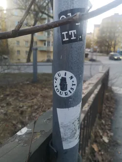Street sticker A circular sticker with a white background featuring a black illustration of a vintage twin-lens reflex (TLR) camera at its center. The camera is depicted from a front-facing perspective, showing its two prominent stacked lenses and a viewfinder. Encircling the camera illustration is black, sans-serif, uppercase text that reads 'RUIN' at the top and 'TOURIST' at the bottom, separated by small dots on either side. The overall design is minimalist and graphic, primarily in black and white.