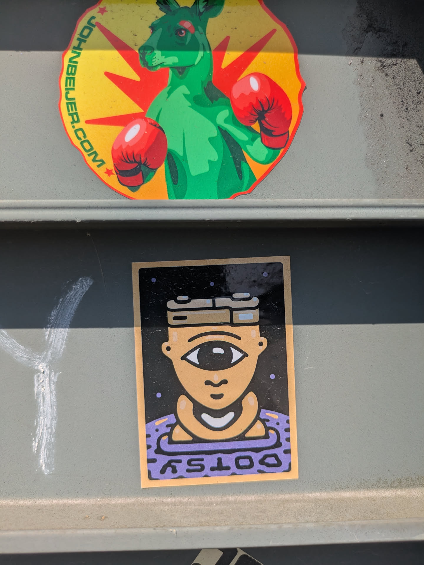 A square sticker with a cyclops-like character. The character has one large eye, and is wearing a purple shirt. The background is black with small dots. The text at the bottom of the sticker reads "DOTSY".