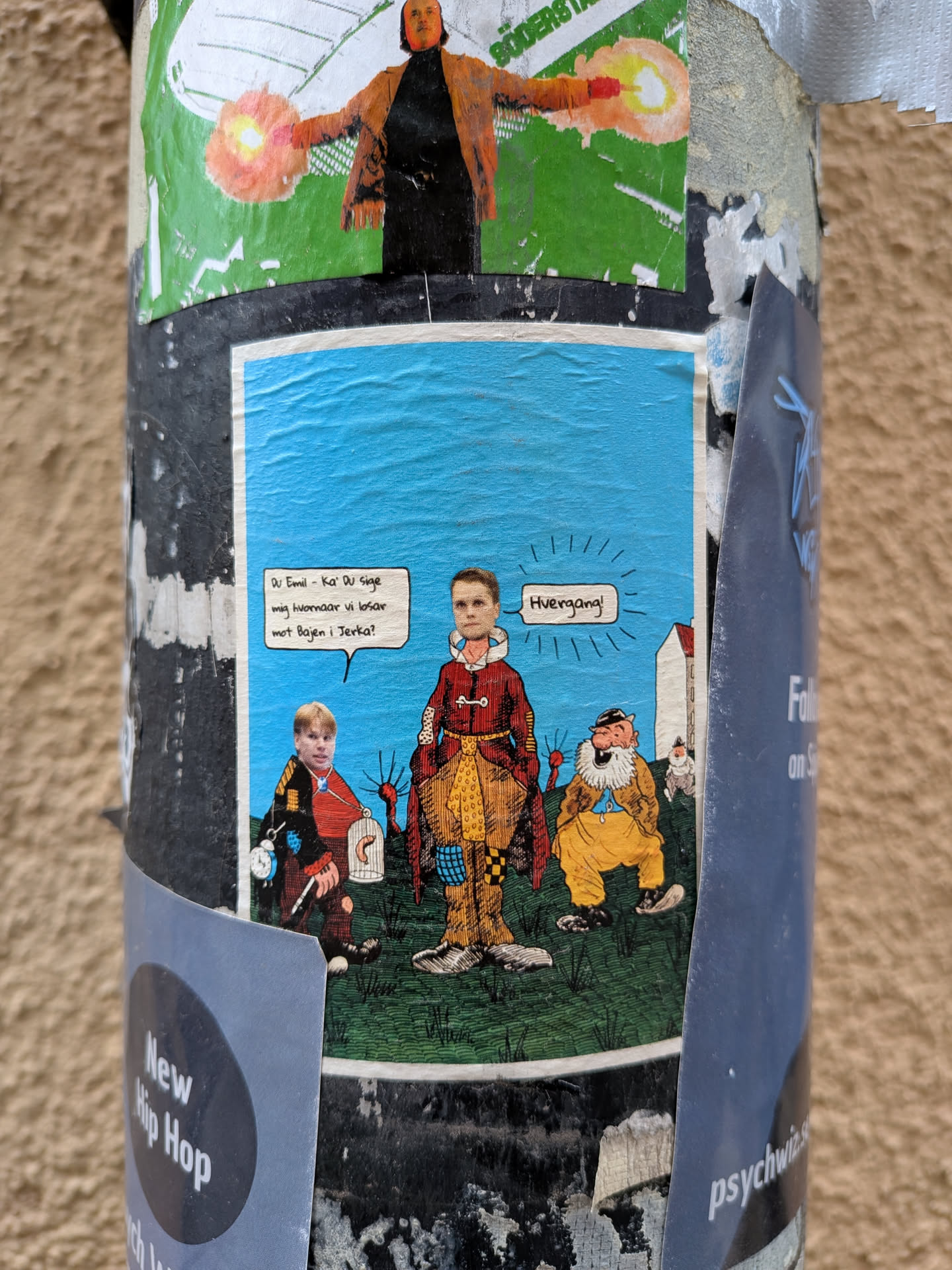 The sticker depicts a light blue sky above a green, grassy landscape. Three figures with realistic faces on cartoon bodies are central to the scene. On the left, a young man in a red and black outfit holds a small birdcage containing a worm and a pocket watch. In the center, another young man, dressed in elaborate red and yellow patterned clothing, stands prominently. To the right, an older, bearded man in yellow pants and a blue shirt sits on the ground. A small white house is visible in the background on the right. Two white speech bubbles contain text in Danish, adding a narrative element to the collage-like illustration.