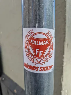 Street sticker A sticker featuring the logo of Kalmar FF, a Swedish football club. The logo is a red and white crest with the words "KALMAR FF" written in the center.  The sticker also features the text "Smålands stolthet" which translates to "The pride of Småland".