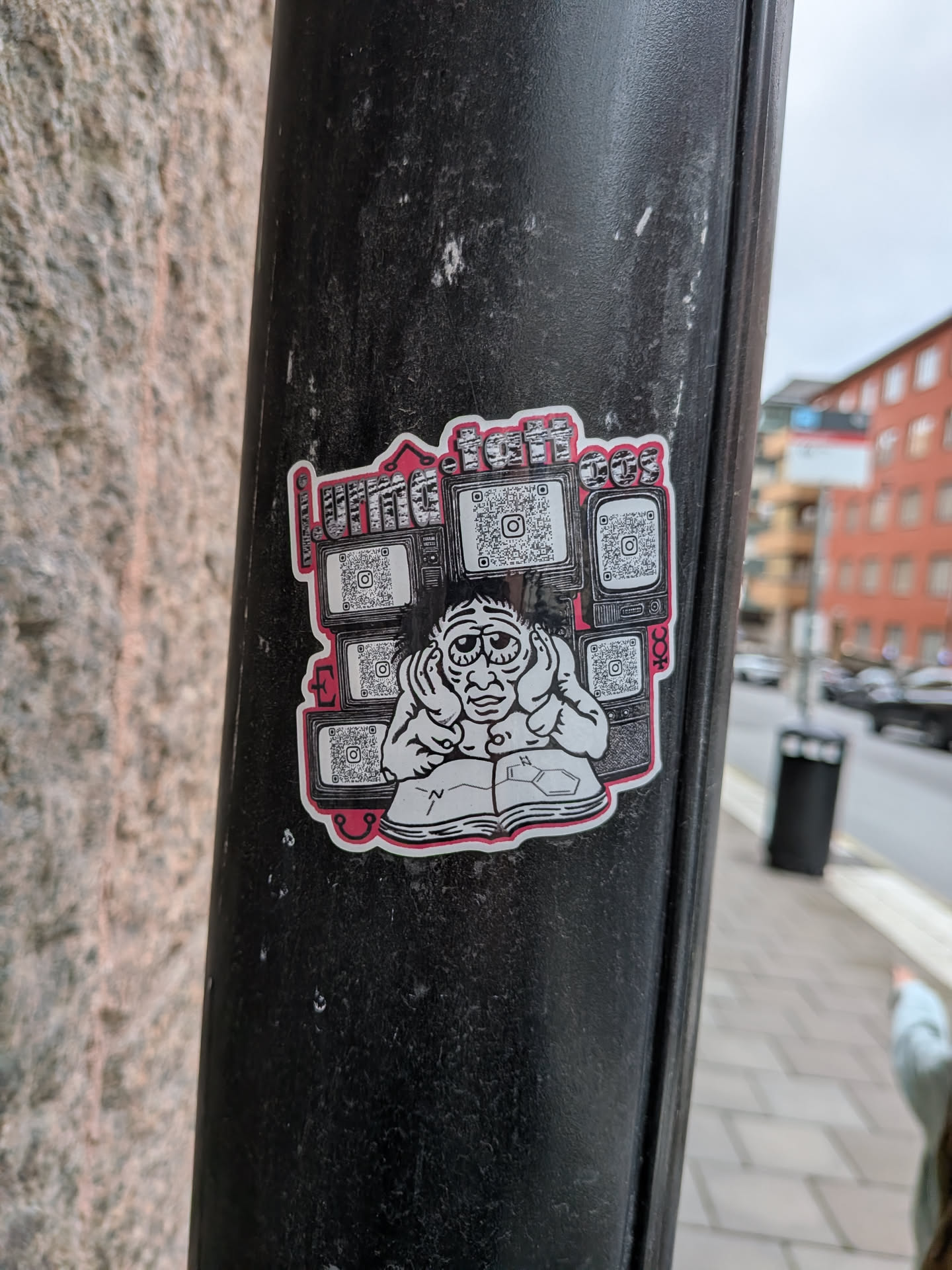 A die-cut sticker with a white border and a thin pink outline. The central illustration features a cartoon character with large, tired eyes, holding their head in their hands while looking down at an open book showing chemical structures. Behind the character are five retro television sets, each displaying an Instagram QR code. Above the TVs, the text 'LIMA.tattoos' is written in a stylized, blocky, textured font. The overall color scheme is black, white, and pink.