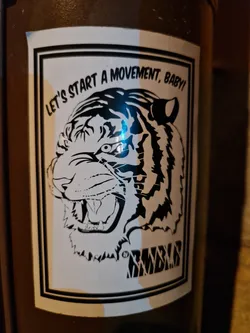 A black and white illustration of a tiger's head with the text 'Let's start a movement, baby!' printed on a white sticker. The sticker has a black border and the word 'ROAR' is printed at the bottom. 