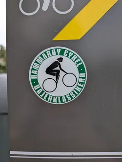 Street sticker A round sticker featuring a green outer ring with the white text 'HAMMARBY CYKEL' and 'BAJENKLASSIKERN'. The white center displays a black stylized icon of a cyclist.