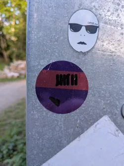 Street sticker A round sticker featuring a purple background split by a horizontal red stripe. A black marker tag is written across the center, with an additional small black mark near the bottom.