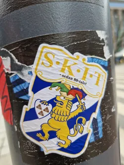 Street sticker A sticker featuring a yellow lion holding a sword, standing on a blue and white shield with three poop emojis. The text 'SKIT - sedan 80-talet' is written at the top. The style is humorous and slightly irreverent.