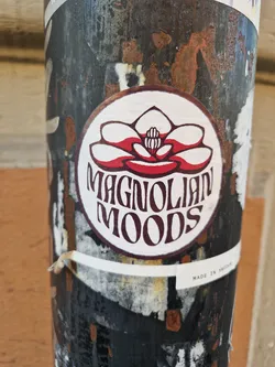 Street sticker A round sticker with a magnolia flower and the text 'MAGNOLIAN MOODS' in a vintage style.  The sticker is affixed to a rusty metal pole.  Small text at the bottom reads 'MADE IN SWEDEN'.
