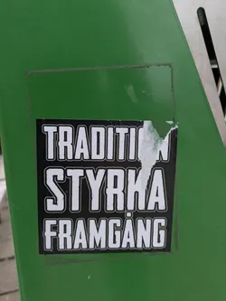 Street sticker The sticker is black and white and has the words "TRADITION STYRKA FRAMGANG" written in capital letters. It is on a green surface, possibly a trash can or similar object.