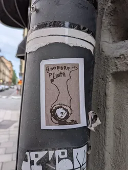 Street sticker Rectangular sticker with a white border and beige background. It displays a black ink drawing of an abstract, eye-like circular figure with wavy lines extending upwards, accompanied by hand-written Spanish text at the top.