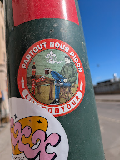 This sticker showcases an illustration of a person seated at a table, enjoying a drink. The sticker is circular with a red border. The text "PARTOUT NOUS PICON" is arched at the top, and "LITTÉ ON TOUR" is arched at the bottom.