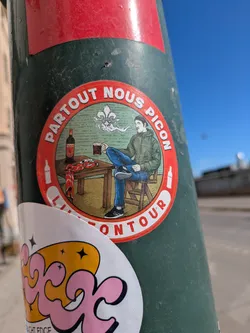 Street sticker This sticker showcases an illustration of a person seated at a table, enjoying a drink. The sticker is circular with a red border. The text "PARTOUT NOUS PICON" is arched at the top, and "LITTÉ ON TOUR" is arched at the bottom.
