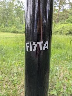 Street sticker A rectangular black sticker featuring the word 'FISTA' in bold, white, stylized capital letters, with the 'S' shaped like a lightning bolt. It is affixed to a glossy black metal pole.