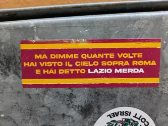 Street sticker The sticker has a red background with yellow stripes on the top and bottom.  It features Italian text: "MA DIMME QUANTE VOLTE HAI VISTO IL CIELO SOPRA ROMA E HAI DETTO LAZIO MERDA", which translates roughly to: "But tell me how many times you've seen the sky above Rome and said Lazio sucks". The sticker is affixed to a grey metallic surface.